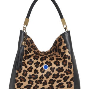 May include: A hobo-style handbag featuring a tan and black leopard print fur-textured centre panel, black leather side panels, a single black leather handle with gold-tone hardware, and a black leather tassel. A small blue circular emblem is centred.