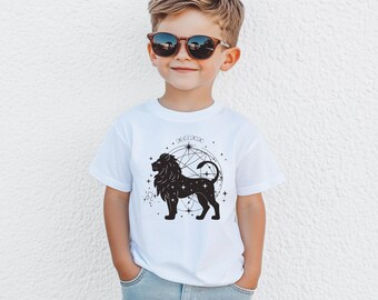 May include: White t-shirt featuring a black lion zodiac design with stars and geometric shapes. The shirt includes the date "26.07.2020" above the lion graphic. The child is wearing sunglasses and blue jeans.