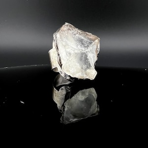 May include: A clear quartz crystal ring with a silver band. The crystal is a rough, natural shape.