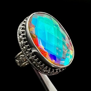 May include: A silver ring featuring a large oval-shaped iridescent gemstone. The gemstone is faceted and displays a rainbow of colours.
