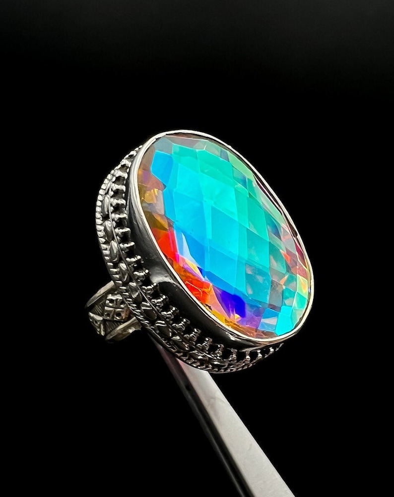 May include: A silver ring featuring a large oval-shaped iridescent gemstone. The gemstone is faceted and displays a rainbow of colours.