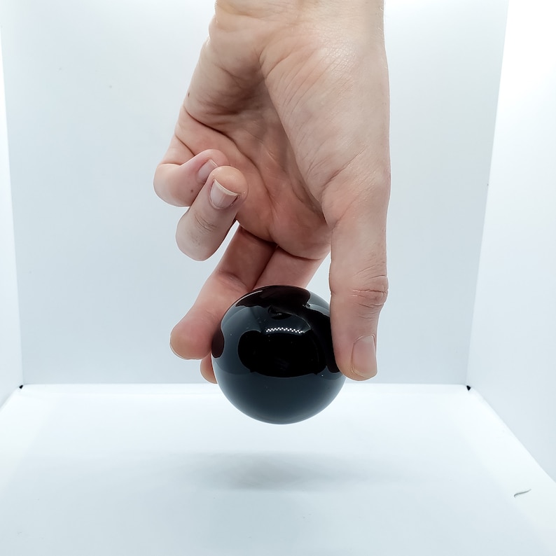 May include: A black glass sphere, held in a hand, with a reflective surface.