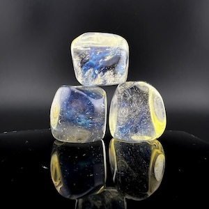 May include: Three clear glass cubes with a blue and yellow swirl pattern. The cubes are stacked on top of each other.