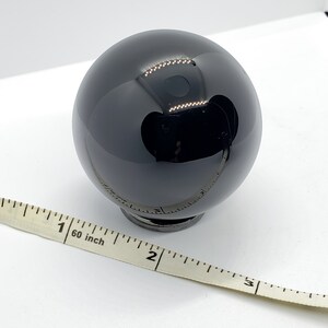 Op de afbeelding: Een zwarte obsidiaans bol, ongeveer 2,5 cm in diameter, rustend op een kleine zwarte basis. Een meetlint ligt op de voorgrond.