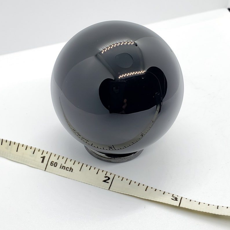 Op de afbeelding: Een zwarte obsidiaans bol, ongeveer 2,5 cm in diameter, rustend op een kleine zwarte basis. Een meetlint ligt op de voorgrond.