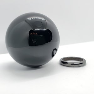 Op de afbeelding: Een zwarte obsidiaans bol en een zwarte obsidiaan ring. De bol is glad en glanzend, terwijl de ring mat is.