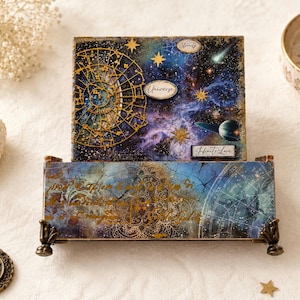 May include: A decorative box with a celestial theme. The box features a galaxy design with gold accents, stars, and the words "Eternity", "Universe", and "Infinite Love". The box is supported by small, ornate feet.