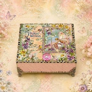 May include: A square decorative box featuring a fairy illustration and the text Fairie Wings on the lid. The box has a pink gingham pattern on the sides, a faceted pink knob, and ornate metal feet. The lid displays flowers and butterflies.