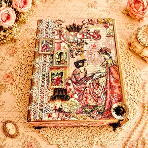 May include: A decorative box with a princess theme. The box features a pink and floral design with the word "PRINCESS" in large letters. It includes lace trim, vintage-style illustrations, and a small carriage charm.