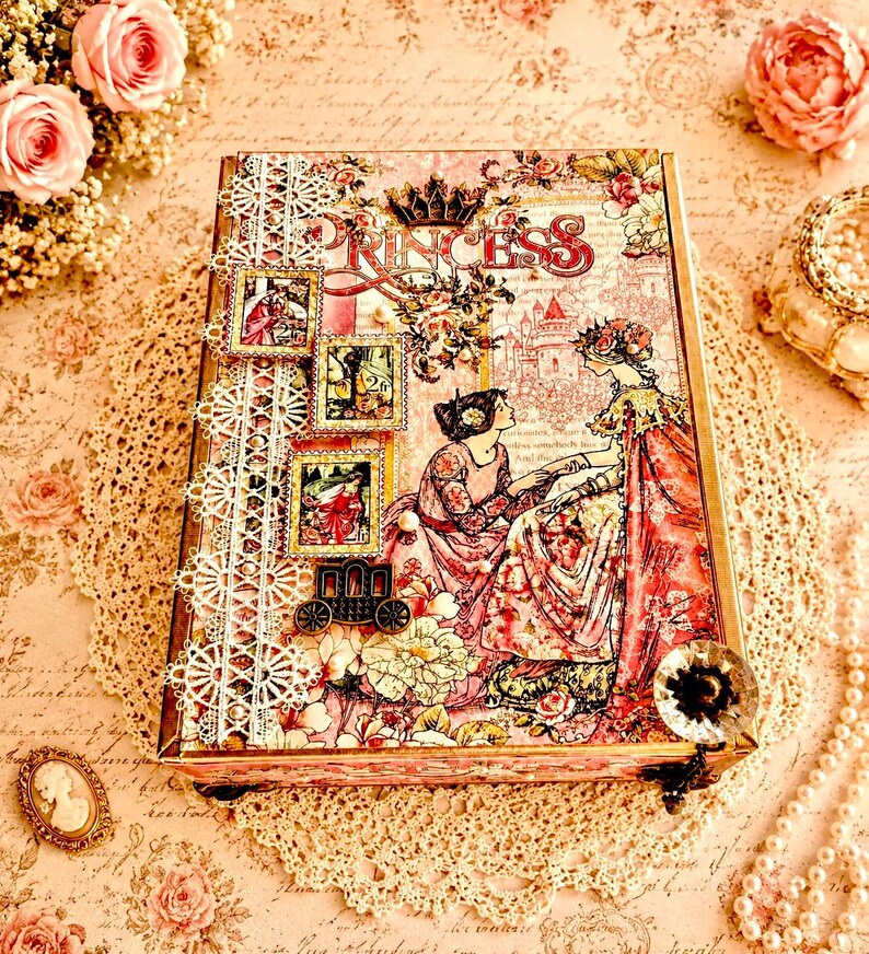 May include: A decorative box with a princess theme. The box features a pink and floral design with the word "PRINCESS" in large letters. It includes lace trim, vintage-style illustrations, and a small carriage charm.