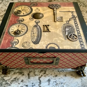 May include: A wooden box with a red and gold patterned lid. The lid features a steampunk design with clocks, gears, and a key. The box has black trim and metal feet.