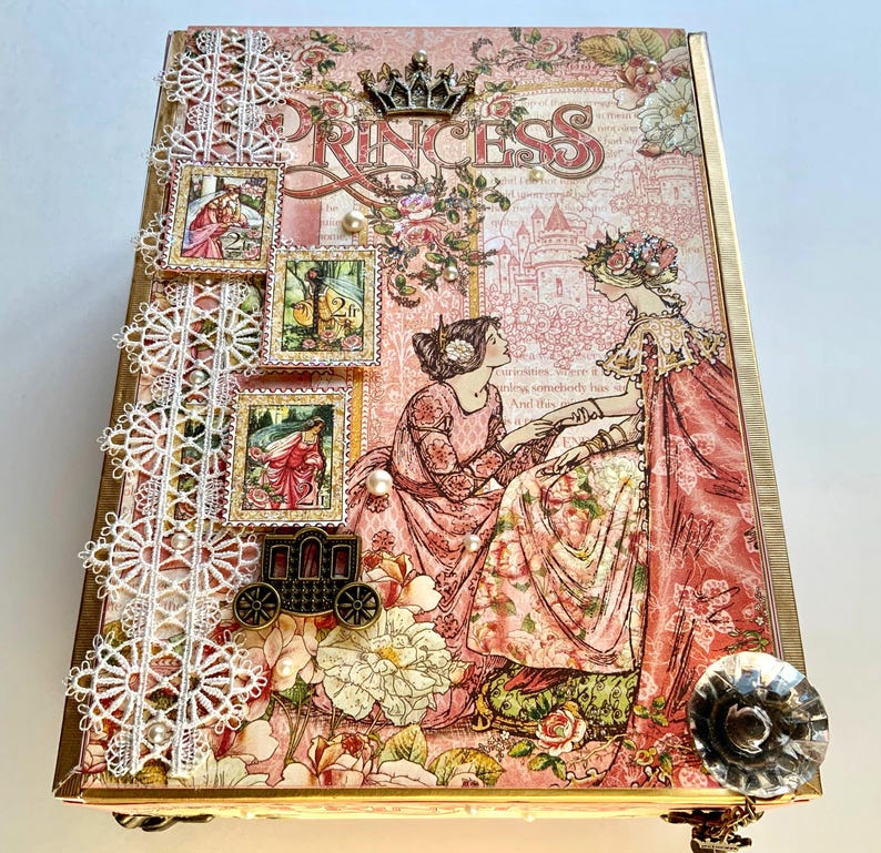 May include: A decorative box with a princess theme. The box features a pink floral design, the word "PRINCESS", and illustrations of women in dresses. Embellishments include lace, pearls, and a carriage charm.