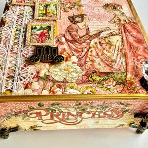May include: A decorative box with a princess theme. The box features a pink floral design, lace trim, and a crystal knob. The word "PRINCESS" is displayed on the front. Decorative stamps and a carriage adorn the top.