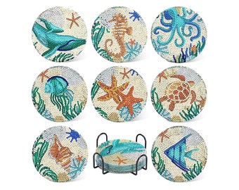 May include: Set of 8 round coasters with a white background and colorful ocean-themed designs. Each coaster features a different sea creature, including a whale, seahorse, octopus, jellyfish, starfish, turtle, seashell, and fish. The coasters come with a metal stand.