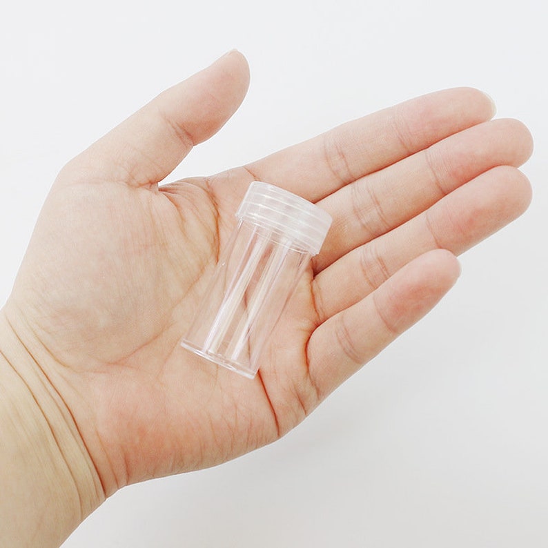 May include: A clear plastic container with a screw-on lid. The container is small and cylindrical.