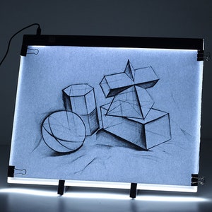 May include: A black light pad with a white surface and a drawing of geometric shapes on it. The light pad is on a black easel and has a cord plugged in.