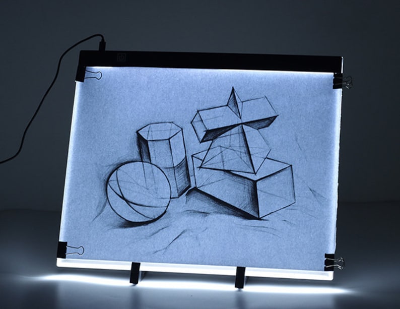 May include: A black light pad with a white surface and a drawing of geometric shapes on it. The light pad is on a black easel and has a cord plugged in.