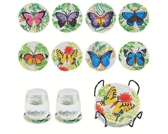 May include: Set of eight round coasters featuring colorful butterfly designs. Each coaster has a green background with a different butterfly design. The coasters are made of a shiny material that resembles rhinestones. The set also includes a metal stand to hold the coasters.