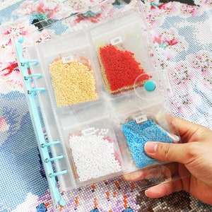 May include: A clear plastic binder with six clear plastic pouches containing small colorful beads. The pouches are labeled with numbers: 715, 350, 05200, 996.