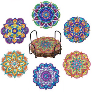 May include: Set of six colorful mandala coasters with a black metal holder. Each coaster features a unique, vibrant design with shades of blue, purple, yellow, orange, and green. The coasters are round and approximately 4 inches in diameter.