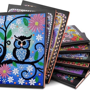 May include: A stack of eight black notebooks with colorful diamond-shaped patterns on the covers. The top notebook features a blue owl on a branch with pink and white flowers.