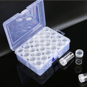 May include: A clear plastic storage box with 36 small clear plastic containers. The box has a hinged lid and a blue latch. The containers are perfect for storing small items like beads, buttons, or jewelry.