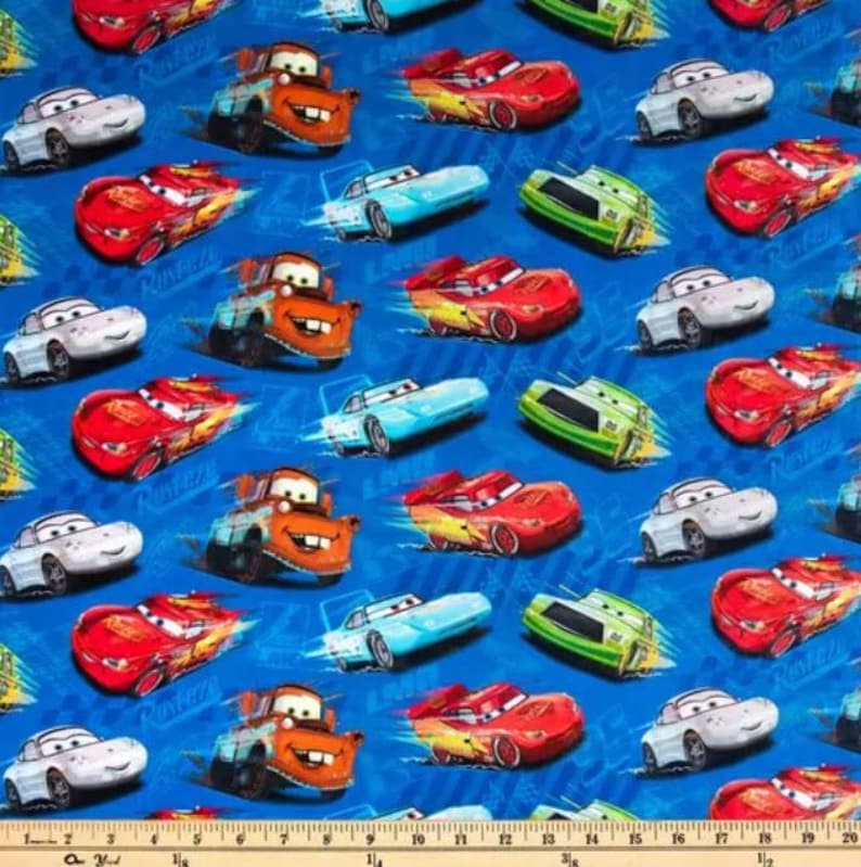 May include: A blue fabric featuring a repeating pattern of cartoon race cars in various colors. The cars include red, white, green, and orange vehicles, with some appearing to be in motion. The background is a solid blue color.