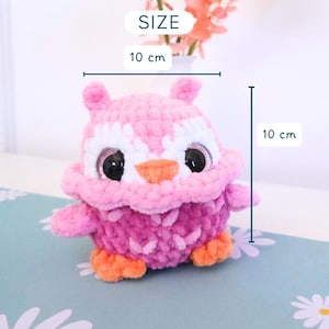 Pu&ograve; includere: Un gufo all'uncinetto rosa e viola fatto a mano, alto 10 cm e largo 10 cm. Il gufo ha grandi occhi neri, dettagli bianchi e zampe e becco arancioni. La parola "SIZE" &egrave; sopra le dimensioni.