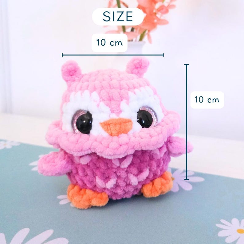Pu&ograve; includere: Un gufo all'uncinetto rosa e viola fatto a mano, alto 10 cm e largo 10 cm. Il gufo ha grandi occhi neri, dettagli bianchi e zampe e becco arancioni. La parola "SIZE" &egrave; sopra le dimensioni.