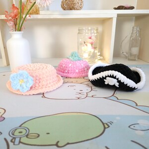 May include: Three crocheted hats in pink, blue and black. The pink hat has white polka dots, the blue hat has a flower, and the black hat has a white skull and crossbones.