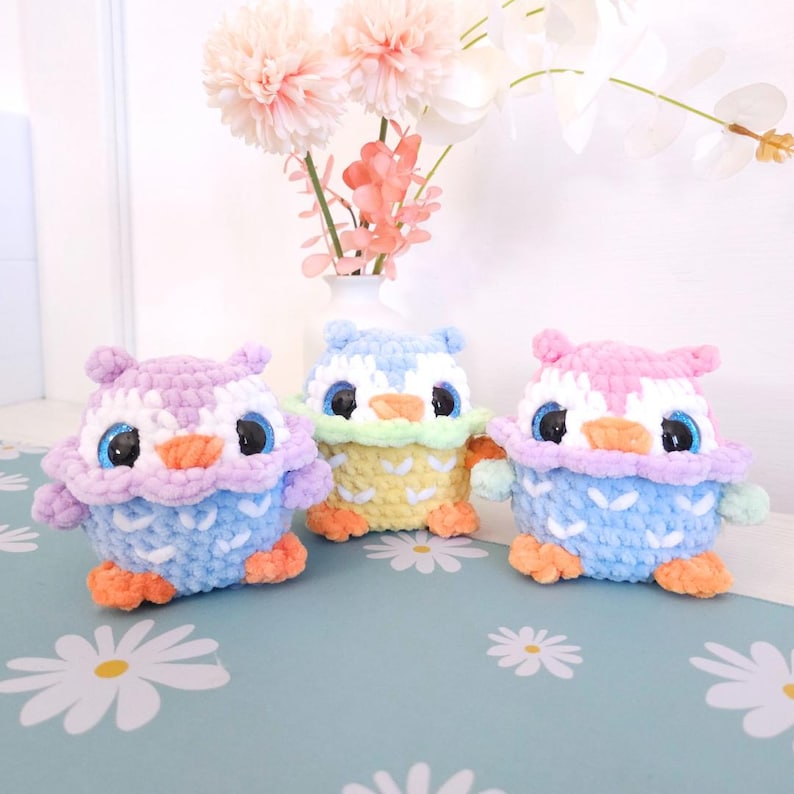 Pu&ograve; includere: Tre figurine di gufo all'uncinetto fatte a mano in colori pastello. I gufi hanno grandi occhi scintillanti e sono nelle tonalit&agrave; di viola, blu, giallo e rosa. Ogni gufo ha una combinazione di colori unica e si trova su una superficie a motivi floreali.