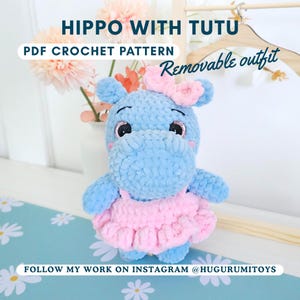 Op de afbeelding: Een handgemaakte blauwe nijlpaardknuffel met een roze tutu en strik. De tekst op de afbeelding luidt "HIPPO WITH TUTU" en "PDF CROCHET PATTERN". De outfit is afneembaar. De Instagram-handle @HUGURUMITOYS is ook zichtbaar.