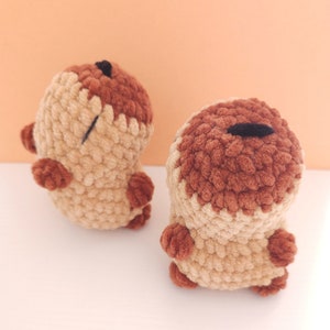 Pu&ograve; includere: Due creature fatte a mano all'uncinetto in marrone chiaro e marrone scuro. Le creature hanno corpi piccoli e arrotondati, braccia e gambe minuscole e un occhio nero. I peluche sono esposti su una superficie bianca.