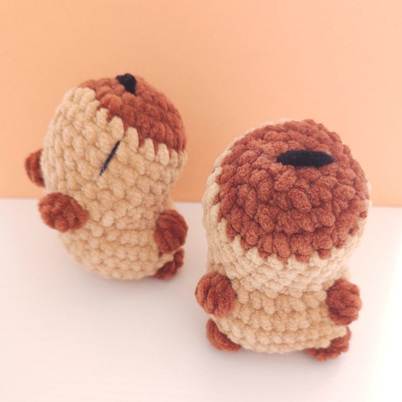 Pu&ograve; includere: Due creature fatte a mano all'uncinetto in marrone chiaro e marrone scuro. Le creature hanno corpi piccoli e arrotondati, braccia e gambe minuscole e un occhio nero. I peluche sono esposti su una superficie bianca.