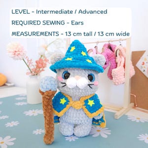 May include: A handmade gray cat plushie wearing a blue wizard hat and cape with yellow star accents. The plushie is holding a brown and blue staff. The text on the image reads: LEVEL - Intermediate / Advanced, REQUIRED SEWING - Ears, MEASUREMENTS - 5.1 inches tall / 5.1 inches wide.