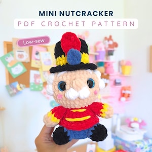 May include: A crochet nutcracker doll featuring a black hat with a red and blue plume, a red jacket with yellow trim, and blue pants. The text MINI NUTCRACKER PDF CROCHET PATTERN and Low-sew are visible above the plush toy.