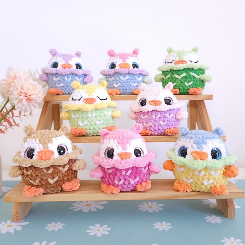 Pu&ograve; includere: Una collezione di figurine di gufo all'uncinetto fatte a mano in vari colori, tra cui marrone, rosa, viola, verde e blu. Ogni gufo ha grandi occhi e una combinazione di colori unica, esposti su una mensola di legno. I gufi sono un affascinante oggetto decorativo.