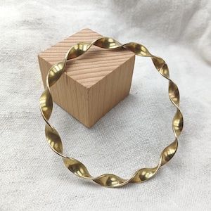 Peut inclure: Un bracelet jonc circulaire en métal doré poli, présentant un design torsadé et spiralé continu qui crée un bord ondulé et sinueux sur toute la circonférence de cette pièce de bijouterie.