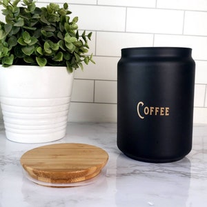 Pode incluir: Um pote de caf&eacute; de cer&acirc;mica preto com tampa de bambu. O pote tem a palavra "COFFEE" escrita em letras douradas.