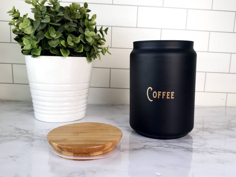 Pode incluir: Um pote de caf&eacute; de cer&acirc;mica preto com tampa de bambu. O pote tem a palavra "COFFEE" escrita em letras douradas.