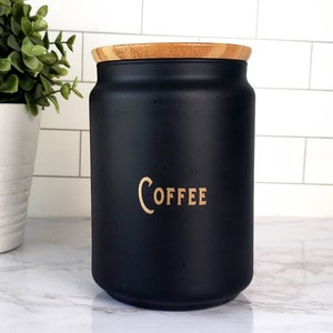 Pode incluir: Um pote de caf&eacute; de cer&acirc;mica preto com tampa de bambu. O pote tem a palavra "COFFEE" escrita em letras douradas.