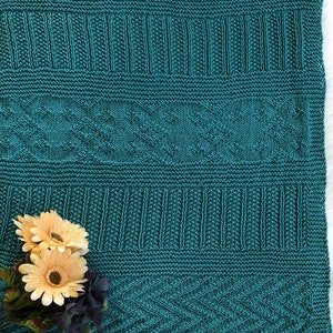 May include: A teal knitted blanket with a geometric pattern. The blanket is made with a textured yarn and has a soft, cozy feel.