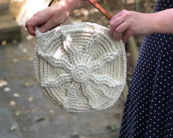 May include: A white crocheted bag with a brown leather strap. The bag has a circular shape with a starburst design.