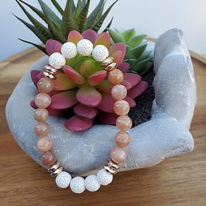 May include: A bracelet made with light brown sunstone beads and white lava rock beads. The bracelet has gold-toned metal spacers.