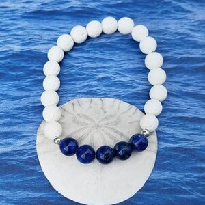 May include: White lava rock beaded bracelet with a row of dark blue lapis lazuli beads in the center.