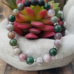 May include: A bracelet made with green, pink, and brown agate beads, black lava rock beads, and silver spacer beads.