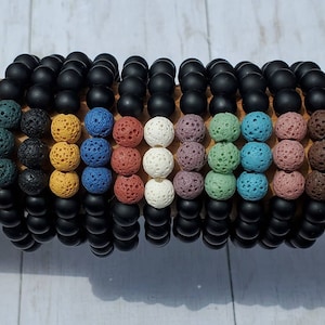 May include: A set of ten bracelets with black lava rock beads and colorful lava rock beads. The bracelets are stacked on top of each other.