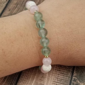 May include: A bracelet with green, pink, and white beads. The beads are made of various materials, including lava rock, rose quartz, and fluorite.