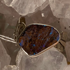 May include: A silver ring with a blue opal stone set in a silver band. The band is decorated with intricate designs.