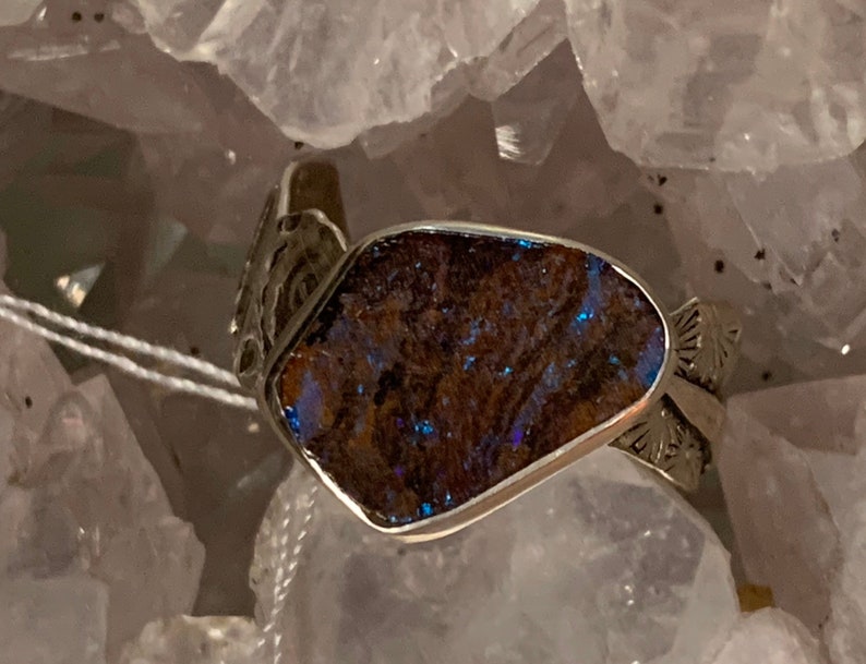 May include: A silver ring with a blue opal stone set in a silver band. The band is decorated with intricate designs.